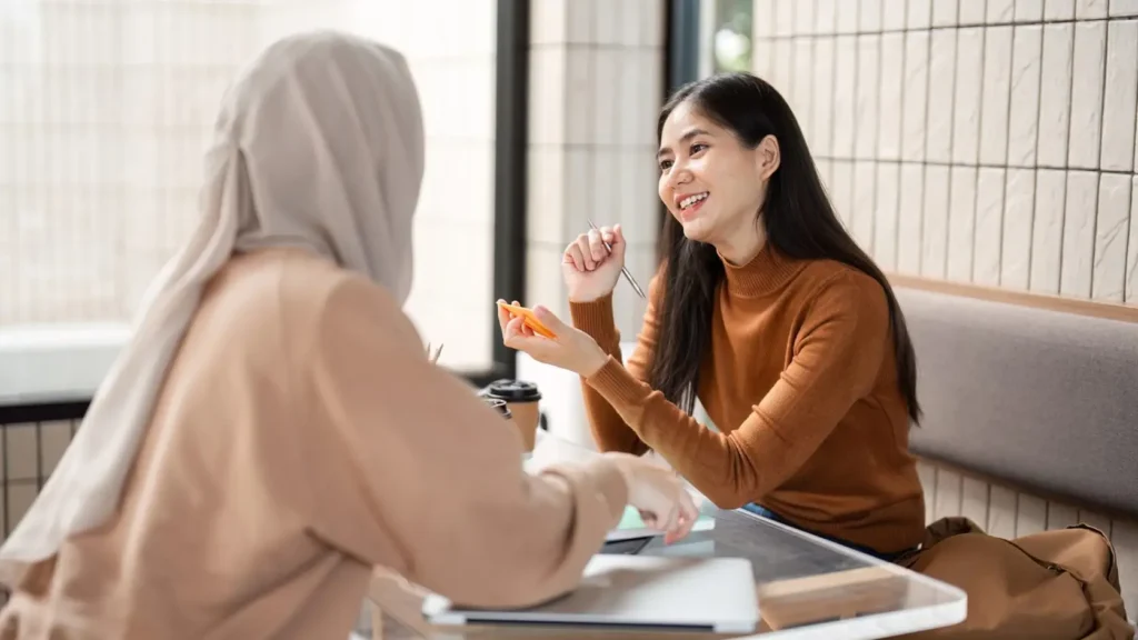 In a casual cafe environment, two friends collaborate on a project, combining their creativity and insights while enjoying coffee.